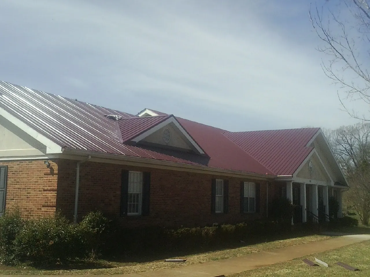 Red metal roof with gabled entries on a long brick building, from a Hail Damage Roof Repair job in Chilo