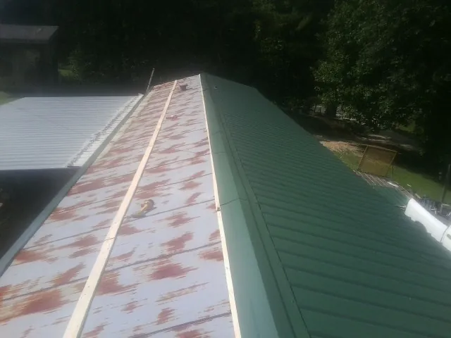 Old rusted panels beside newly installed green metal roofing — Wind Damage Roof Repair by Roofing Brothers in Chilo