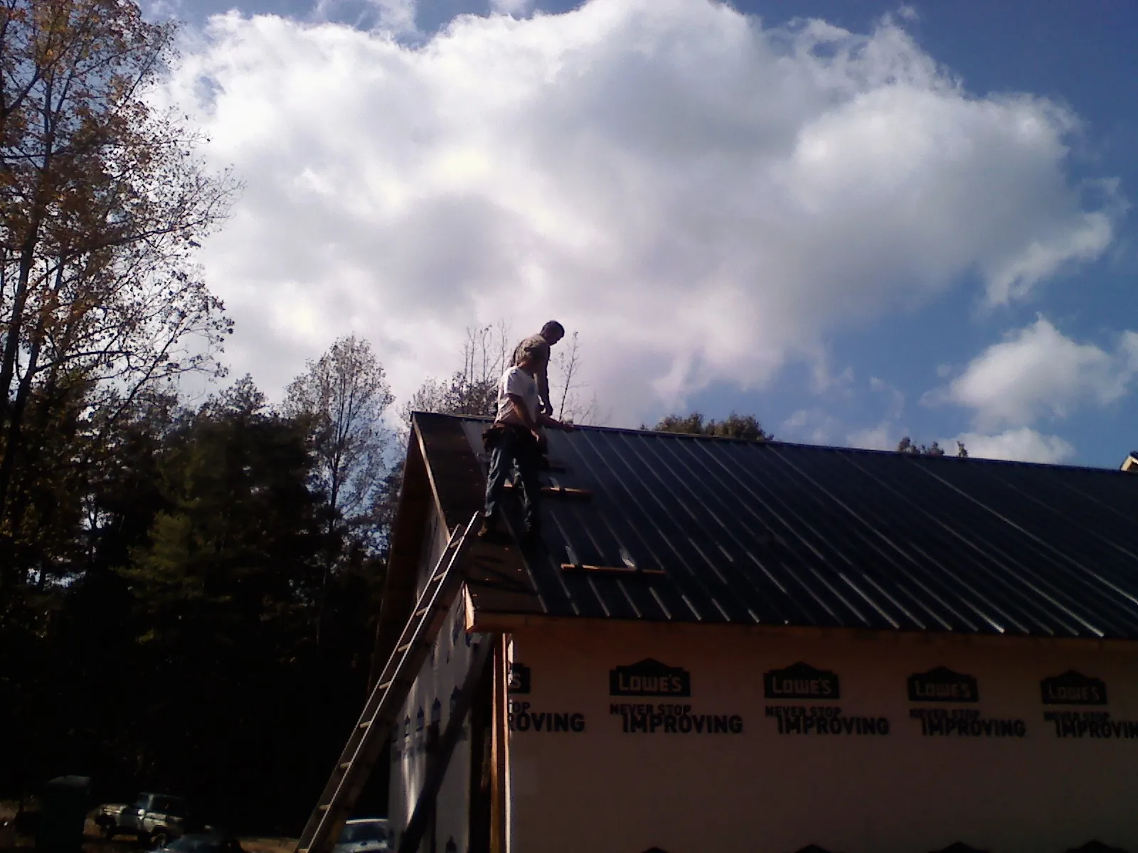 Roofer fastening dark metal panels high against a cloudy sky, from a Roof Inspection job in Chilo